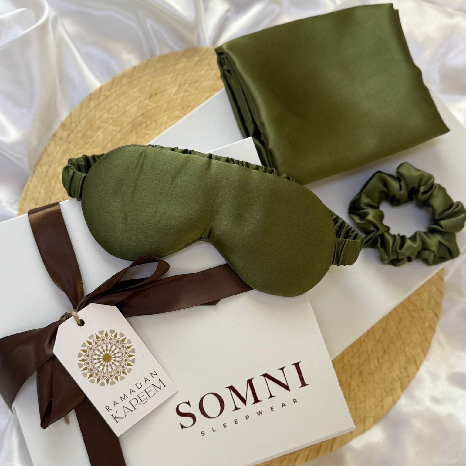 Green satin sleep mask, pillow, and hair tie set with 'SOMNI' branding on a white background.
