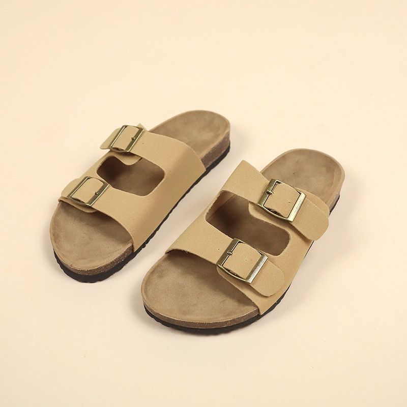 Pair of beige sandals with gold buckles on a beige background