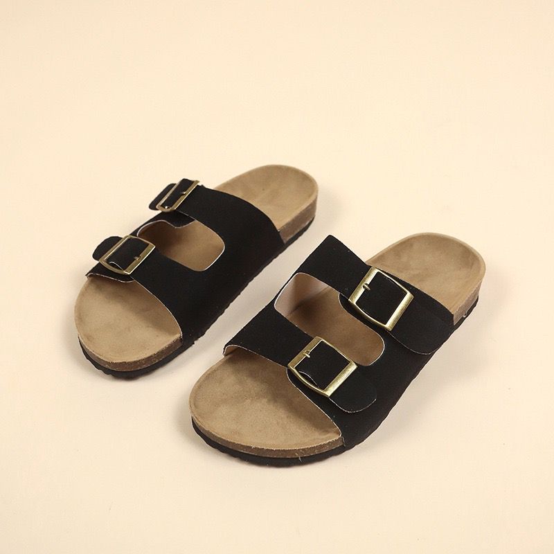 Pair of black sandals with gold buckles on a beige background