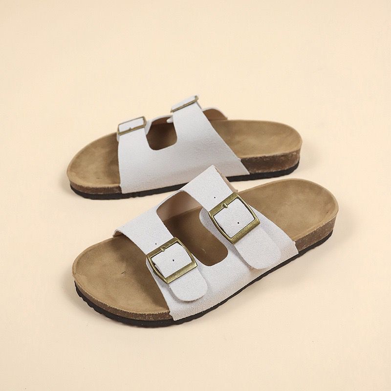 Pair of white sandals with brown soles on a beige background