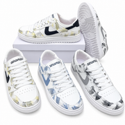 Four low-top Nike sneakers with a white base and tropical leaf print in various colorways, arranged on a white background with one shoe on a white box.