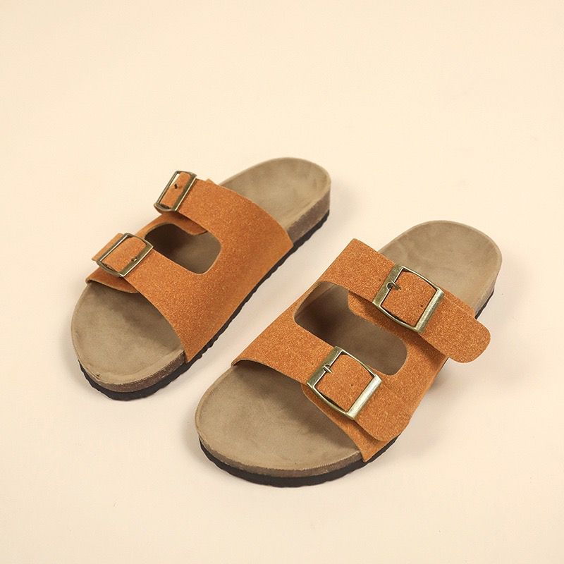 Pair of brown sandals with gold buckles on a beige background