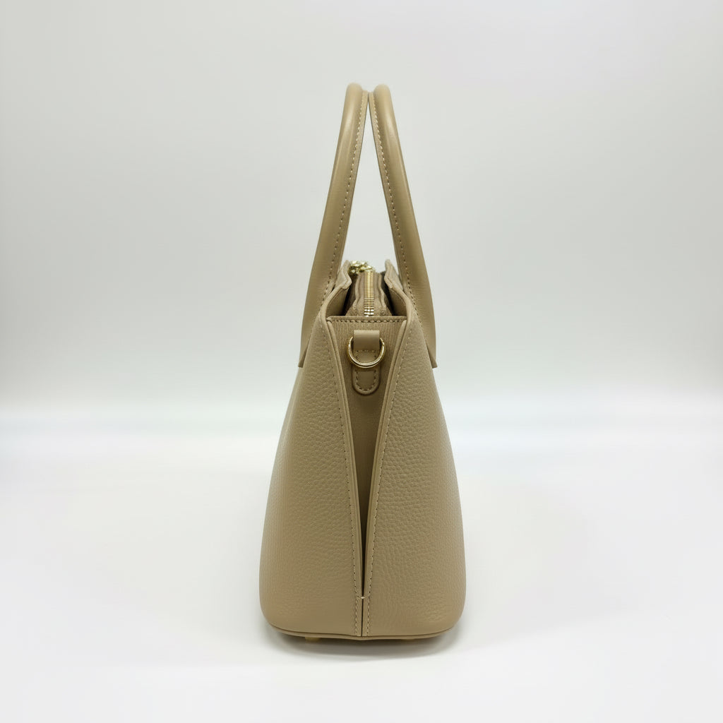 Beige handbag with gold accents on a white surface with a blurred background