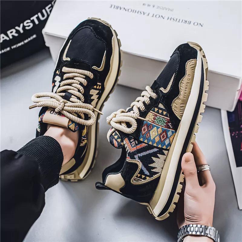 Black and gold sneakers with geometric pattern held by a person on a light gray surface.