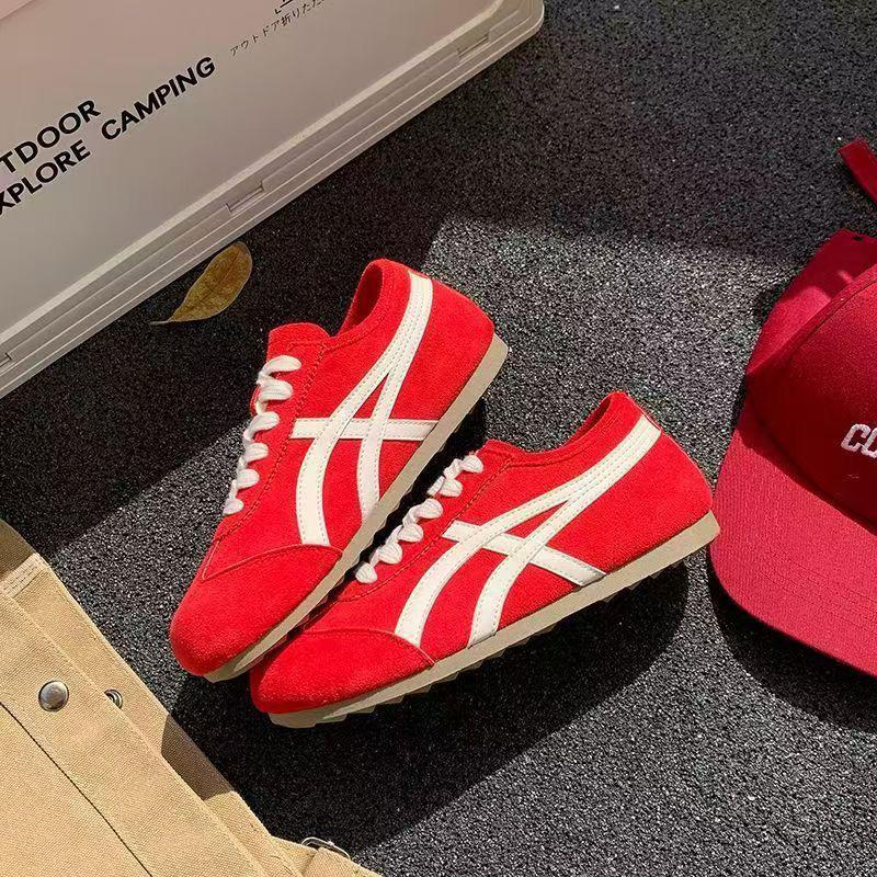 Red sneakers with white accents on a dark surface next to a red cap and beige bag.