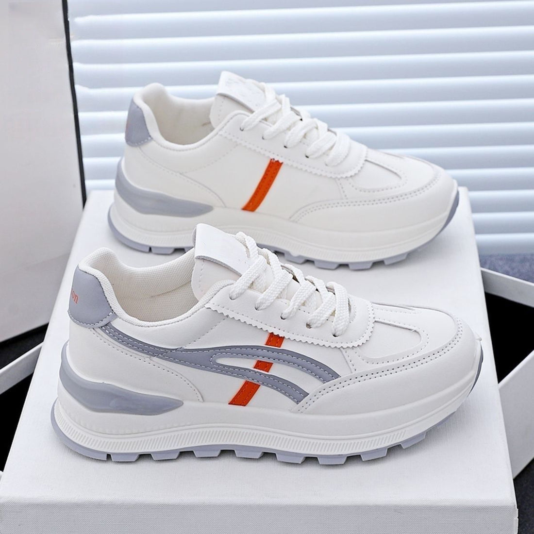 White sneakers with gray and orange accents on a white surface.