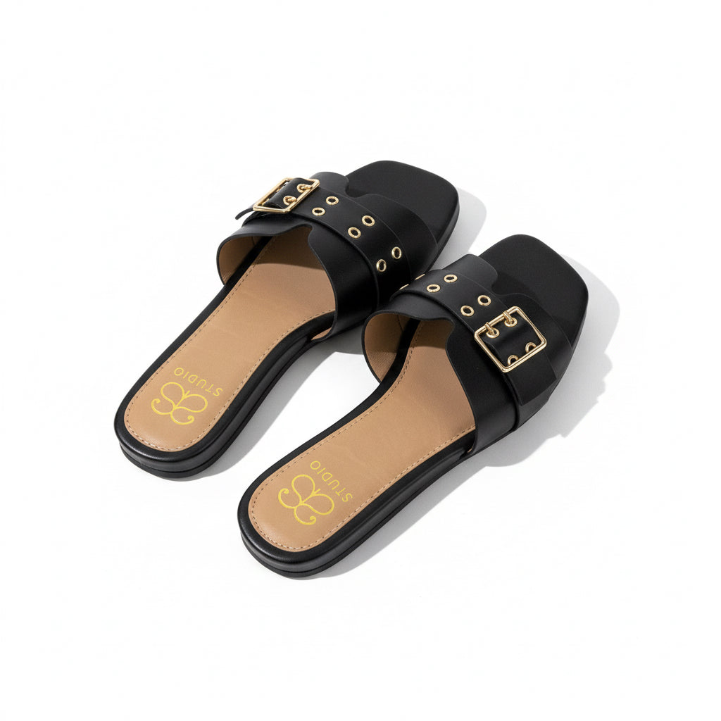 Black sandals with gold buckles on a light wooden floor.
