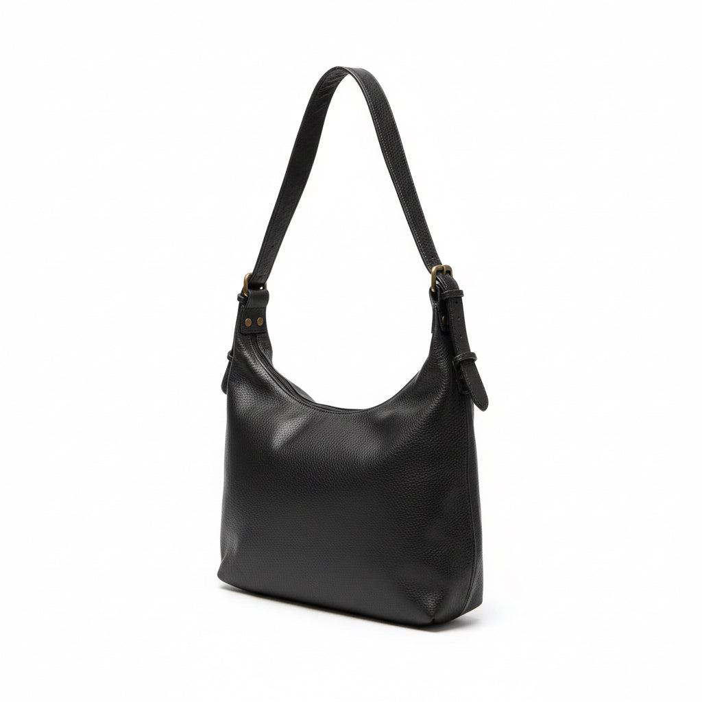 Black leather handbag on a wooden surface next to a laptop, with a light-colored wall and power outlet in the background.