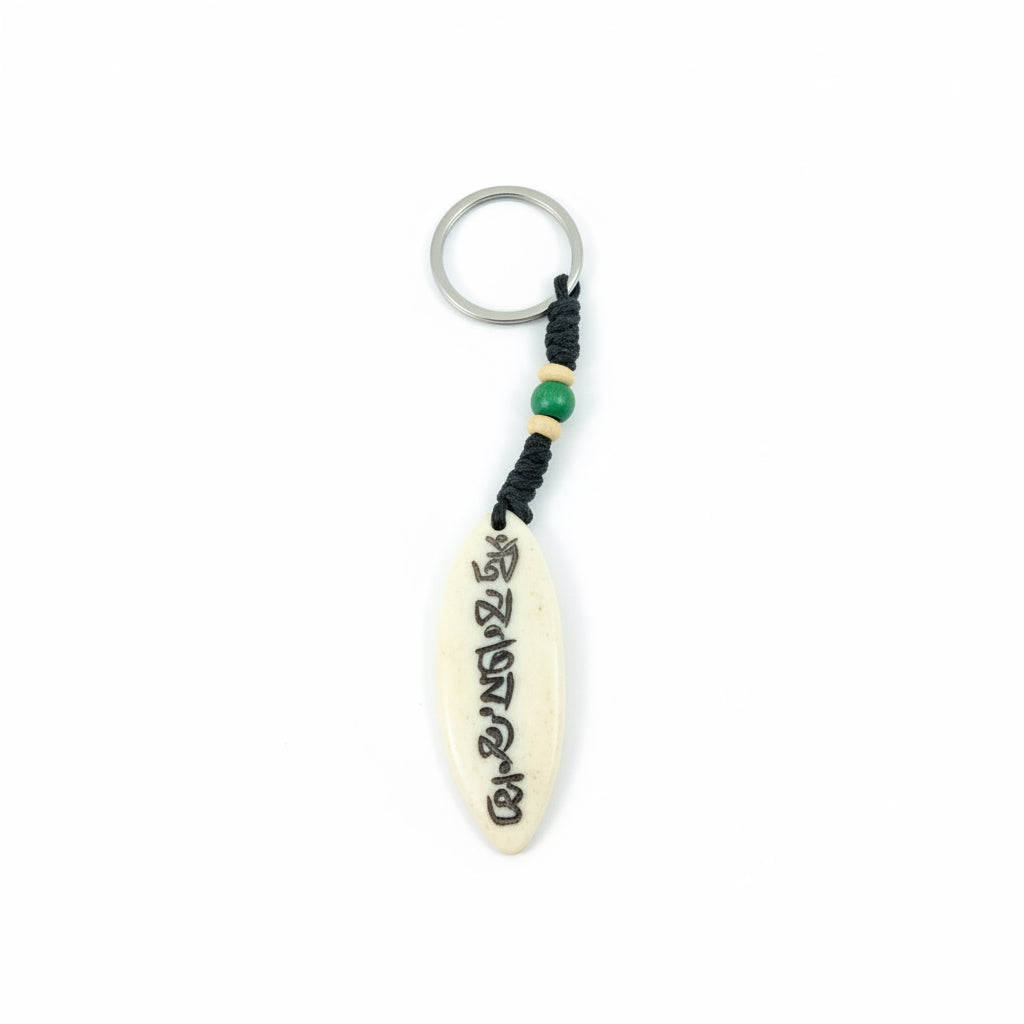 Leaf-shaped yak bone keychain engraved with Om Mani Padme Hum mantra in Tibetan script with green bead detail.