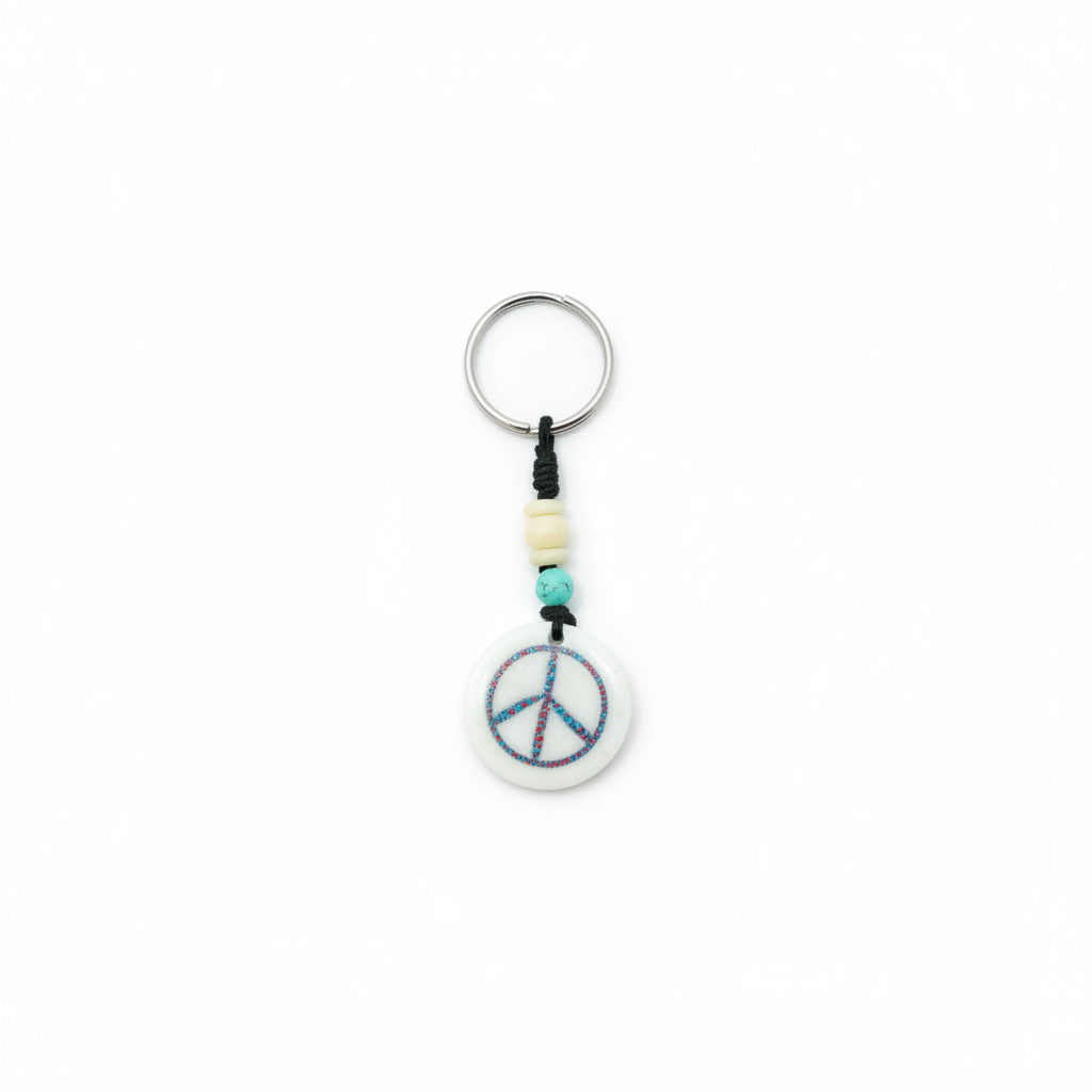 Circular yak bone keychain with a hand-carved peace sign and colorful inlay on a black braided cord.
