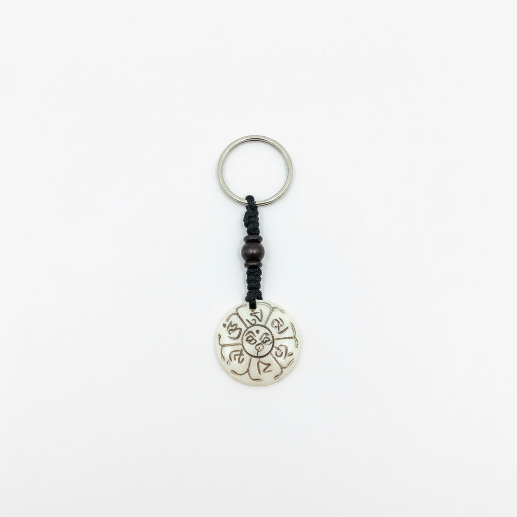 Circular yak bone keychain with hand-carved Kalachakra Wheel of Time symbol and dark wooden bead.