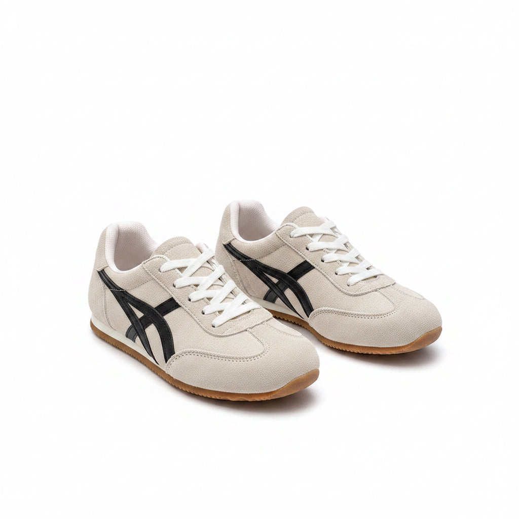 White sneakers with black accents worn by a person on a dark floor.