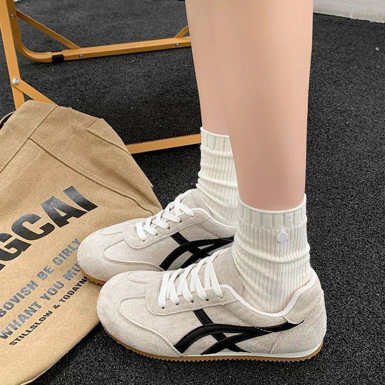 White sneakers with black accents worn by a person on a dark floor.