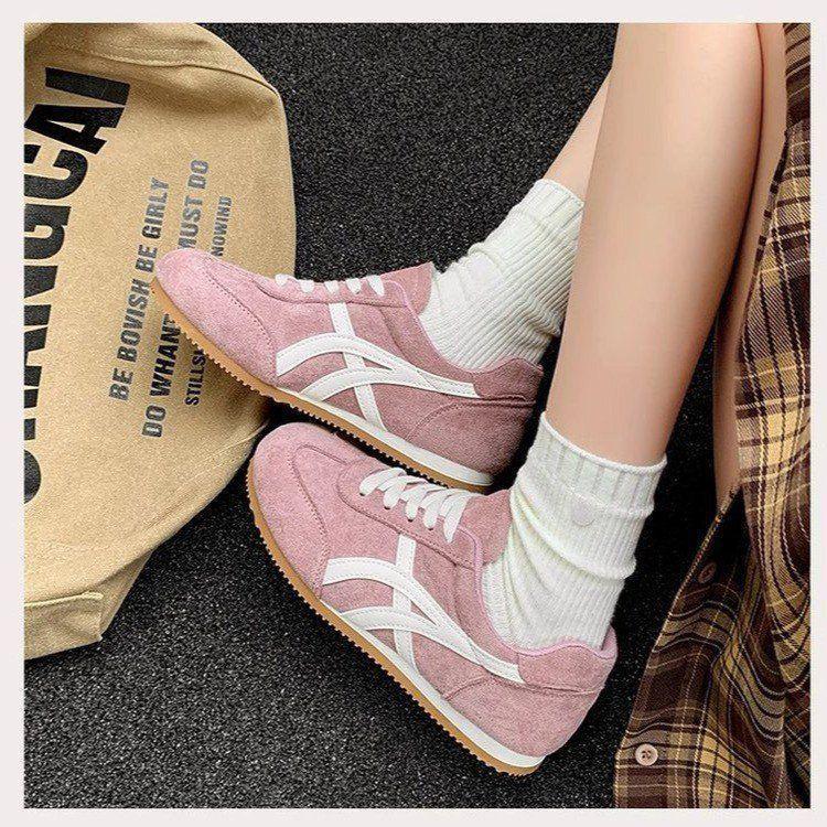 Pink sneakers with white accents worn by a person, with a beige bag and plaid fabric in the background.