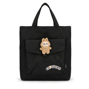 Black canvas tote bag front view featuring front flap pocket with plush character charm and Capybara text patch
