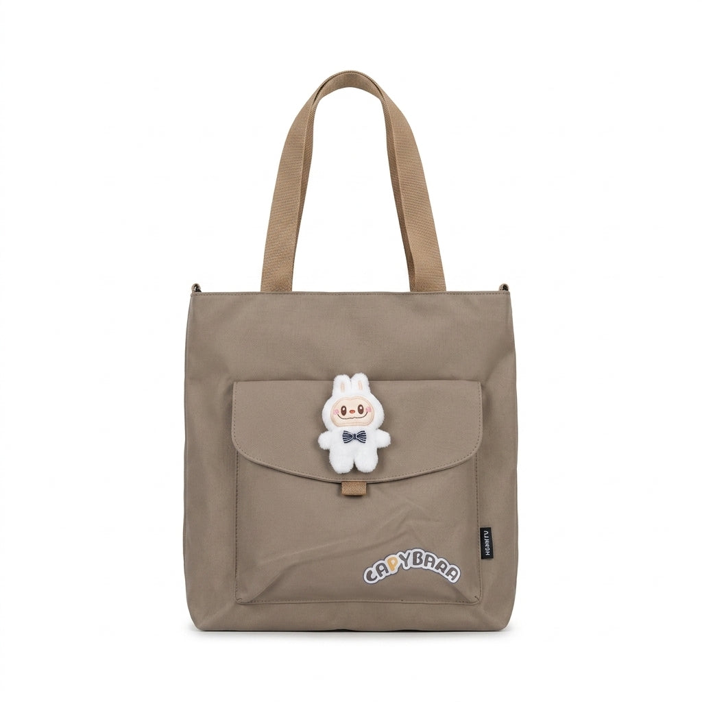 Khaki canvas tote bag front view featuring front flap pocket with plush character charm and Capybara text patch accent