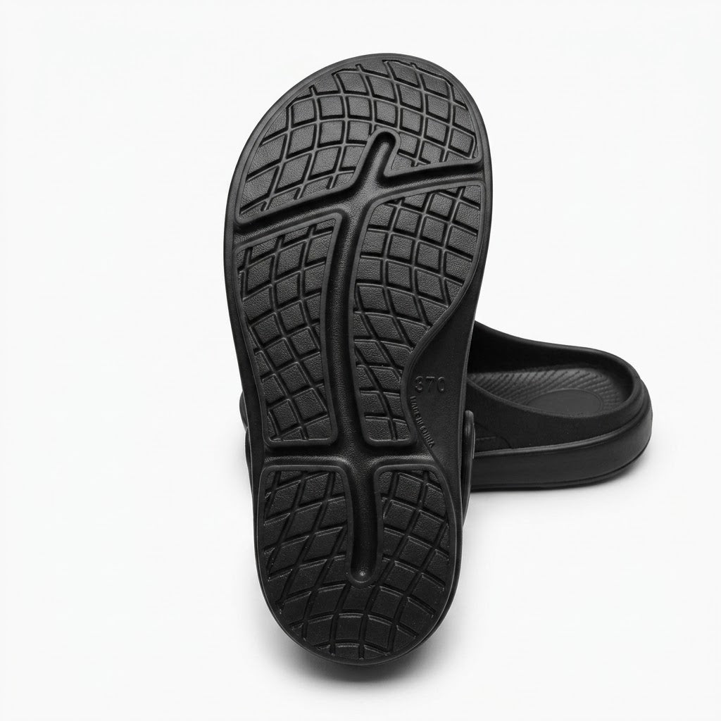 Black molded clog-style shoe shown from the sole side, with a textured tread pattern and a second shoe partially visible behind it on a clean white background.