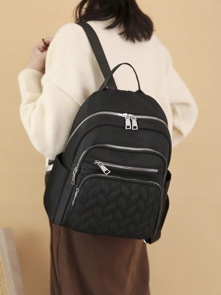 Black quilted backpack with silver zippers worn by a person against a beige background