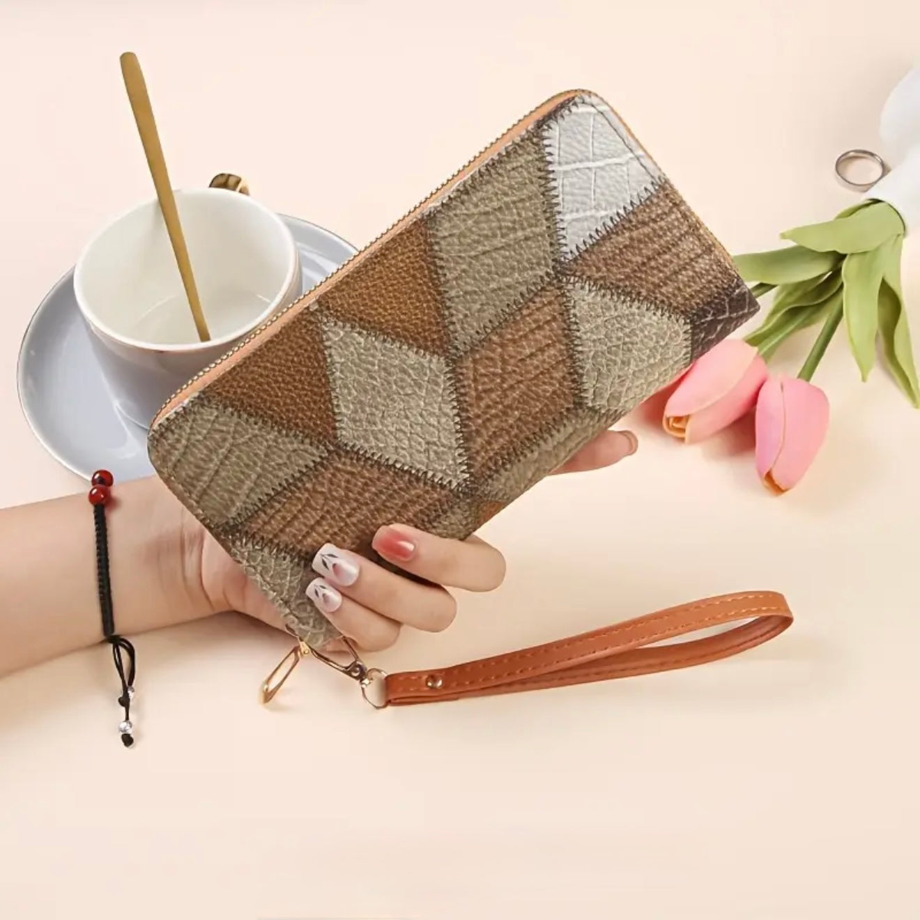 Woman holding a brown textured geometric patterned zip-around wallet with attached wristlet strap