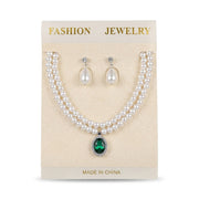Women's double strand faux pearl necklace featuring an oval green gemstone pendant with matching pearl drop earrings on display card.
