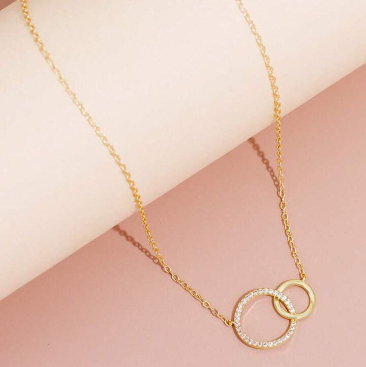 Gold necklace with interlocking rings on a pink background