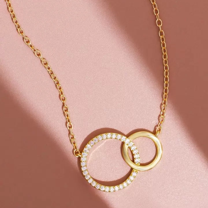 Womens gold interlocking double circle pendant necklace featuring one rhinestone studded ring and one polished ring on a link chain