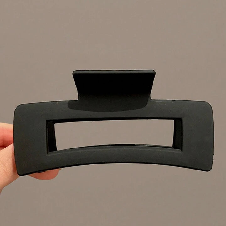 Black hair clip held by a hand against a plain background