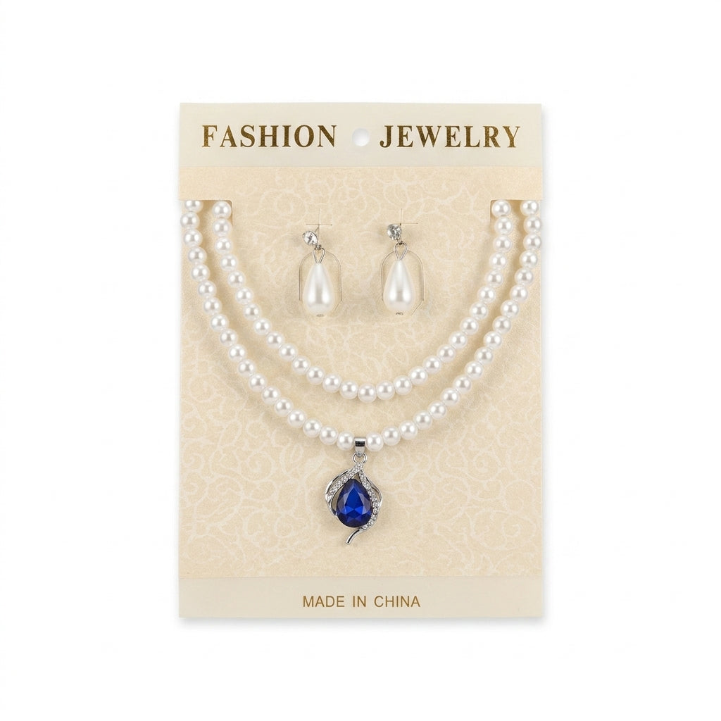 Women's white faux pearl necklace with blue teardrop pendant and matching drop earrings set on display card